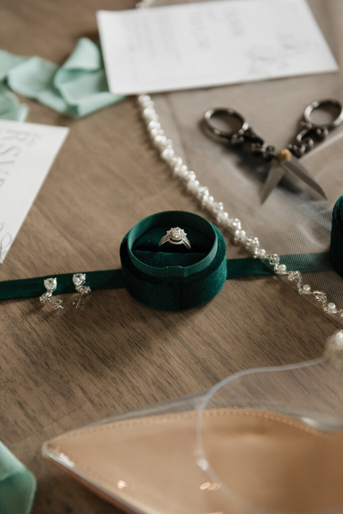 Emerald green ring box with a diamond ring in the middle, surrounded by other wedding day details