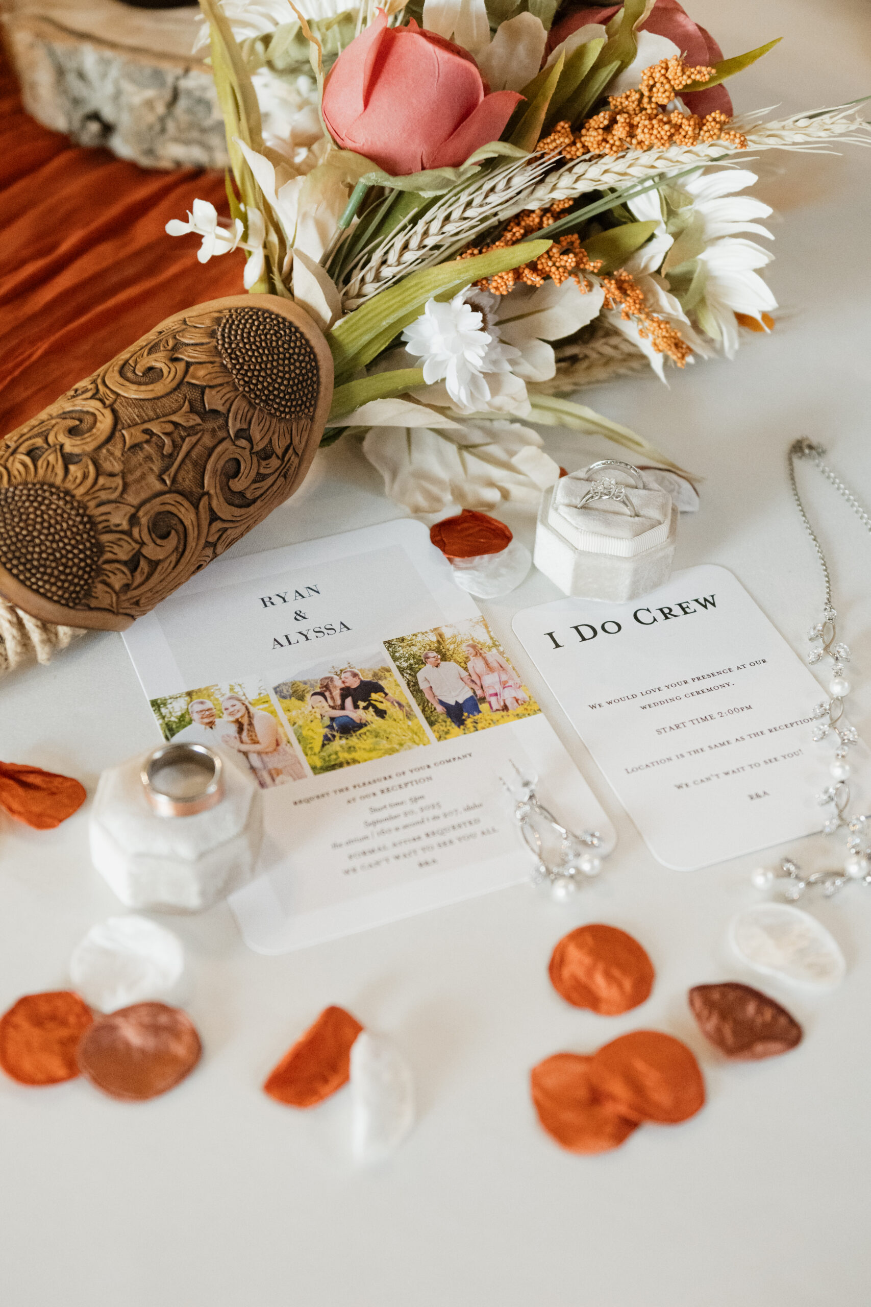 Rustic wedding detail flatlay setup with flowers, rings, an invitation suite, and the bride's wedding jewelry.